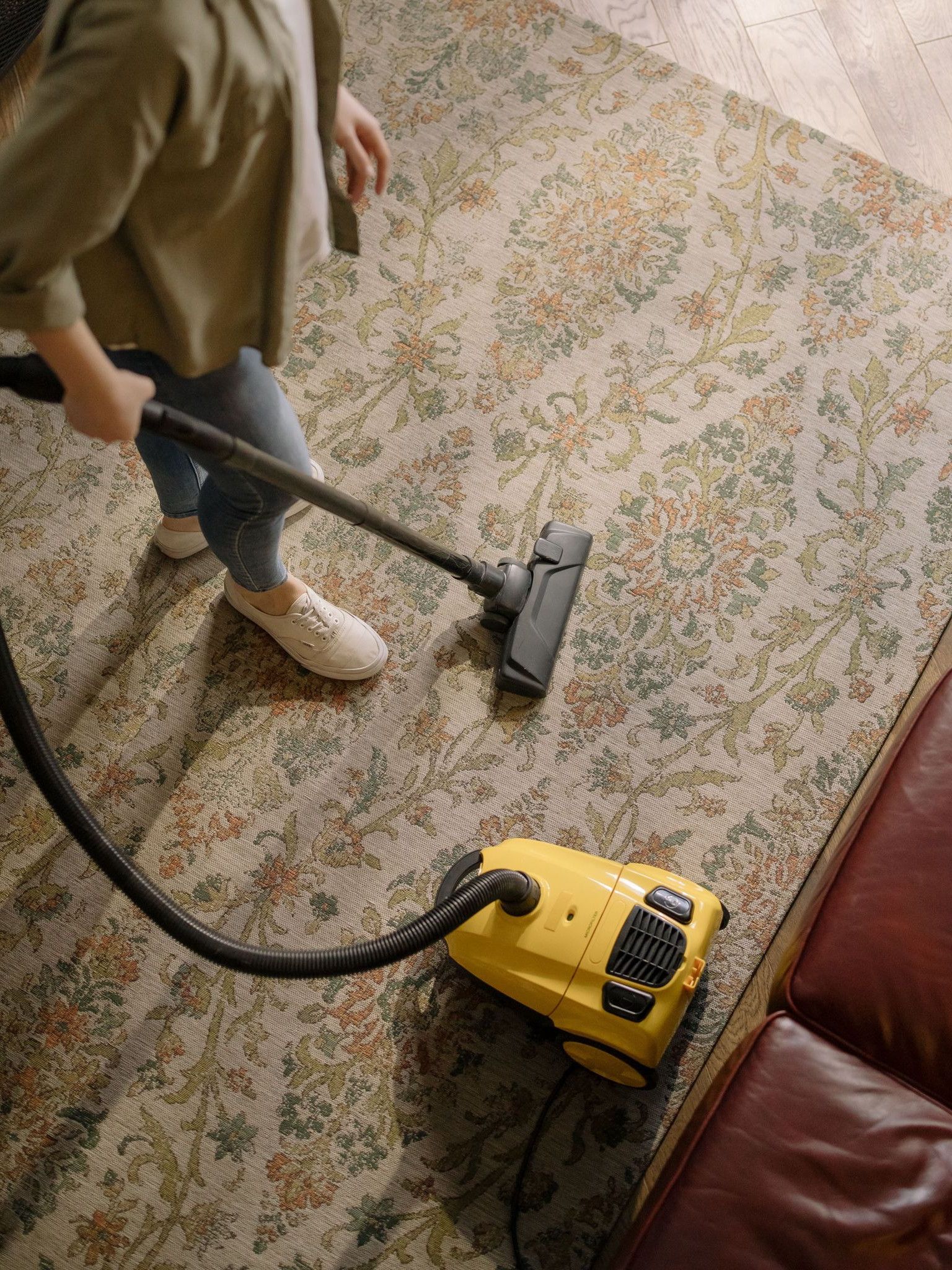 Overhead view of a woman vacuuming a carpet at home, highlighting cleanliness and housekeeping.