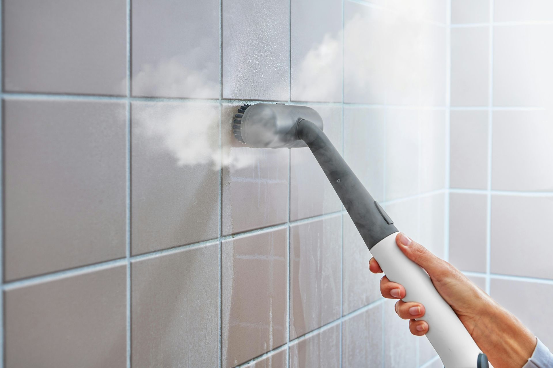 Steam cleaner sanitizing tiled wall in bathroom